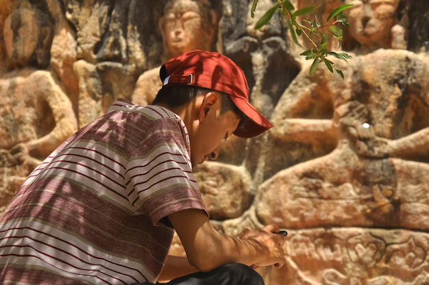 Man observing ancient Buddha carvings on a rock wall.
