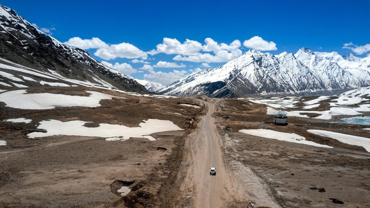 Snow-covered mountains and road at Chang La Pass with a car driving through