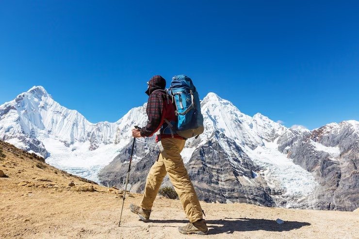 Trekker with backpack walking towards snow-covered mountains in Ladakh