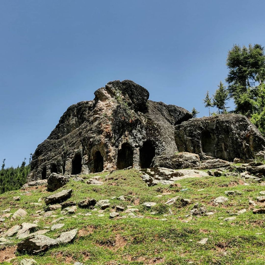 Rocky entrance of Kalaroos Caves surrounded by greenery in Kashmir