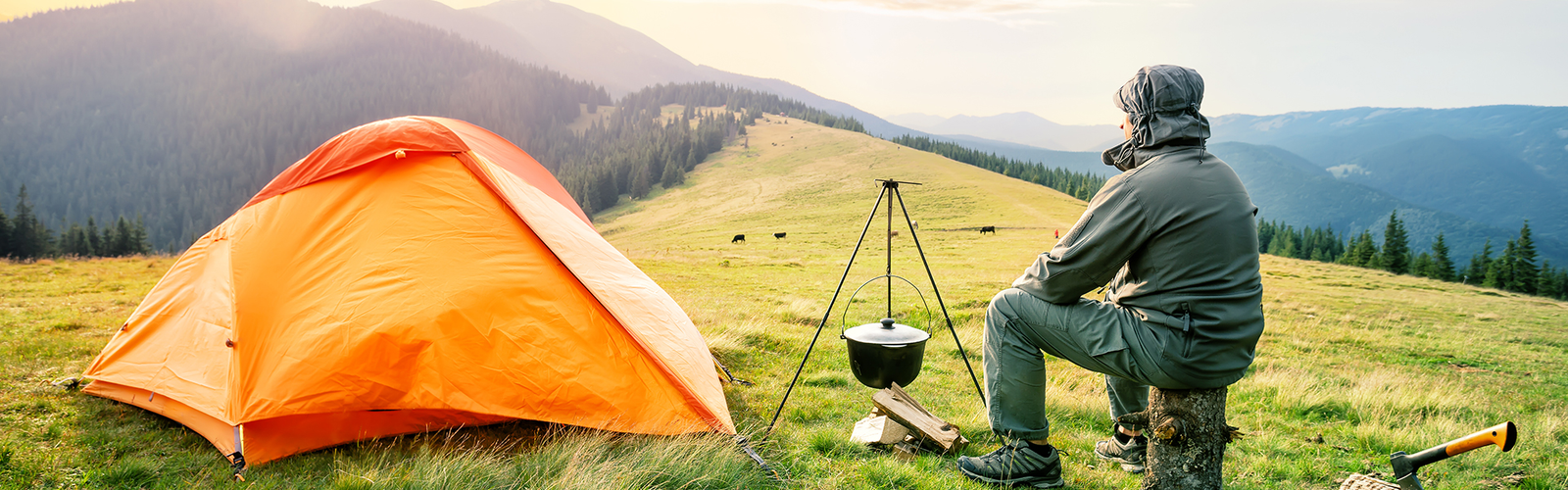 Camping in Kashmir with a bright orange tent and a hiker cooking outdoors amidst scenic mountain views.